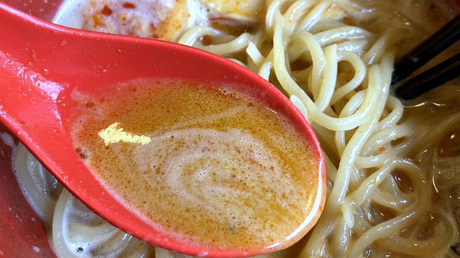 赤いレンゲですくった濃厚なラーメンのスープ