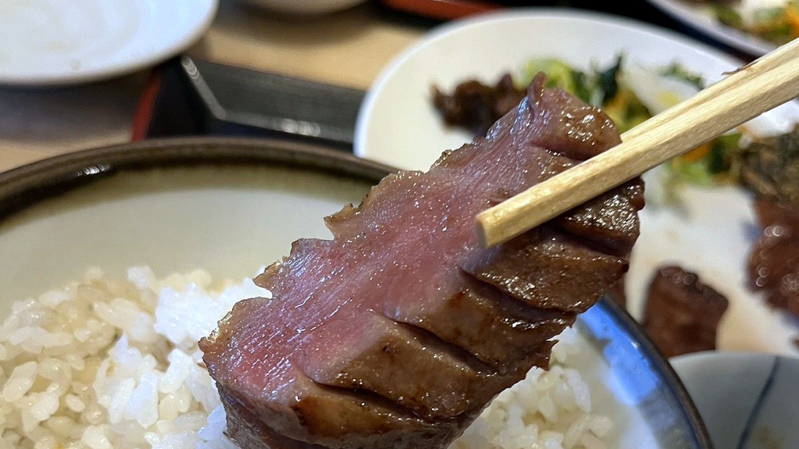 麦飯の上に箸で持ち上げられた厚切り牛タン